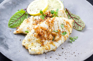 Fried calamari tubes in breadcrumbs breading with lemon slices and lettuce leaves offered as closeup on a modern design plate